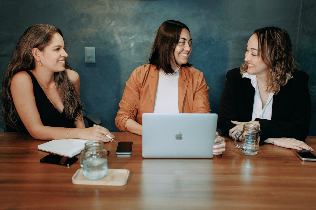 Three women engaged in a professional meeting with a laptop and notes, fostering teamwork and collaboration.